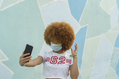 Woman with afro hair and mask taking a selfie with her smartphone