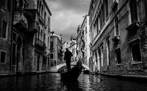 Rear view of gondolier sailing boat in canal amidst buildings