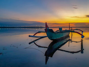 Fishing boat moored at beach against sky during sunset