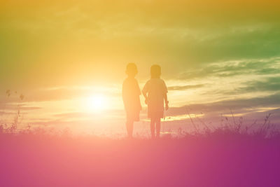 Silhouette friends standing against orange sky