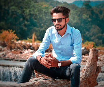 Man wearing sunglasses while sitting on fallen tree trunk