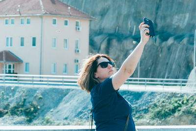 Woman wearing sunglasses taking selfie while standing outdoors