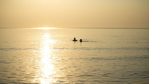 Silhouette people on sea against sky during sunset