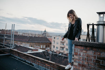 Smiling young woman standing against cityscape during sunset