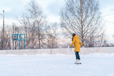 Young woman in yellow jacket skating at the rink