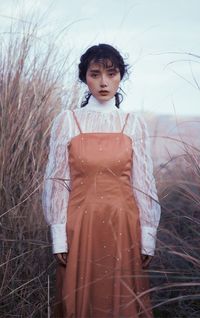 Portrait of young woman standing by plants against sky