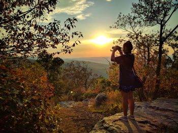 Rear view of woman photographing at sunset