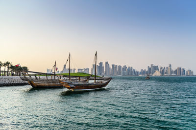 Sailboats in sea by buildings against clear sky