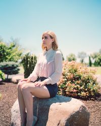 Young woman sitting on rock against clear sky