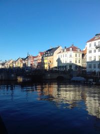 Buildings by river against blue sky