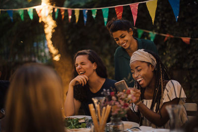 Cheerful multi-ethnic friends enjoying at table during dinner party in backyard