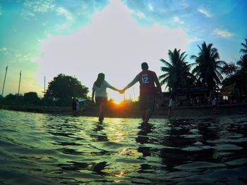 People by swimming pool against sky during sunset