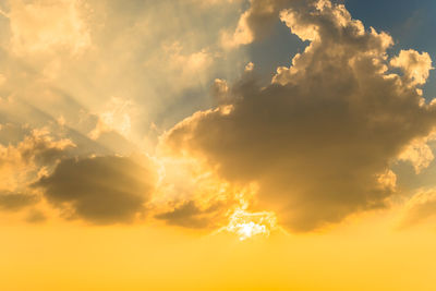 Low angle view of sunlight streaming through clouds during sunset