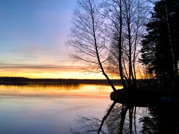 Silhouette bare trees by lake against sky during sunset