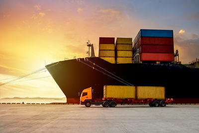 Truck receive containers from large ship with sunset background