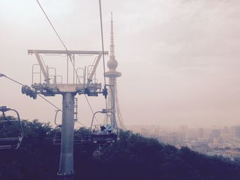 Ski lift towards communication tower in city against sky