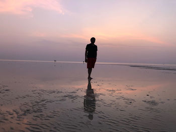 Rear view of person standing on beach during sunset