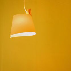 Low angle view of illuminated lamp against yellow background