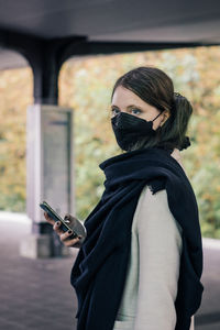 Young woman using mobile phone, wearing mask