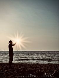 Rear view of man standing at beach against sky during sunset