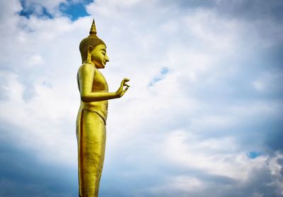 Low angle view of golden buddha statue against cloudy sky