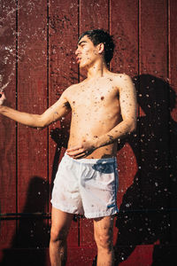 Shirtless man splashing water on himself against wall