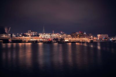 Illuminated city by sea against sky at night