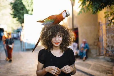 Smiling woman with macaw on head at street