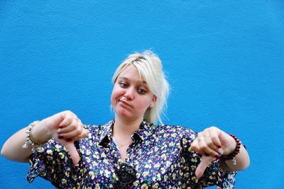 Woman gesturing thumbs down against blue wall