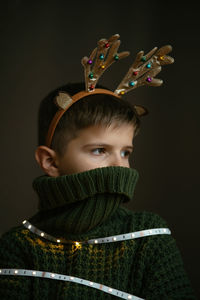 Boy with deer horns for christmas, hides his face in a collar as in mask