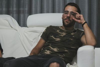 Portrait of handsome young man in eyeglasses sitting on sofa at home