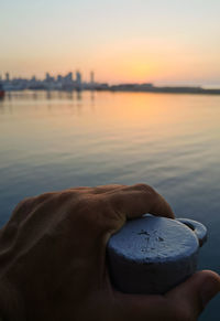 Midsection of person holding sea against sky during sunset