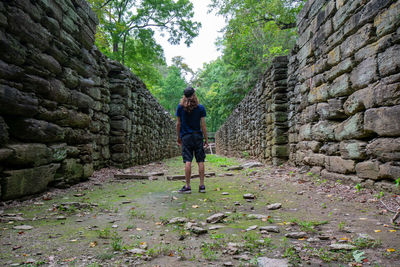 Rear view of man standing amidst ancient built structure in forest