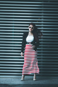 Young fashionable woman standing on footpath against wall