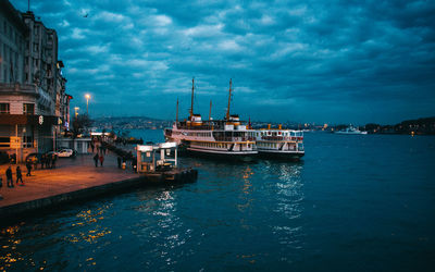 Boats moored at harbor against cloudy sky at dusk
