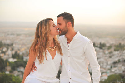 Young romantic couple kissing while sitting against cityscape