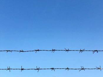 Low angle view of barbed wire against clear blue sky