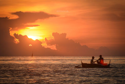 Silhouette people in sea against sky during sunset