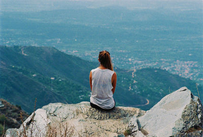 Rear view of woman sitting on mountain top