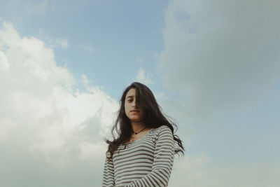 Low angle view of young woman standing against sky