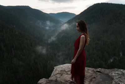 Rear view of woman standing on cliff against mountain