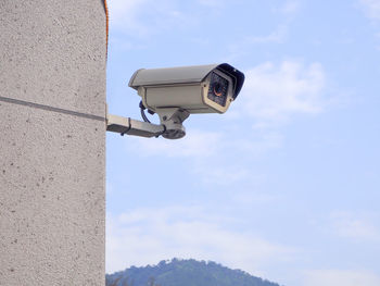 Low angle view of security camera on wall against blue sky