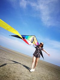 Tilt image of woman with colorful kite standing at beach against blue sky