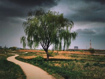 Road passing through field against cloudy sky