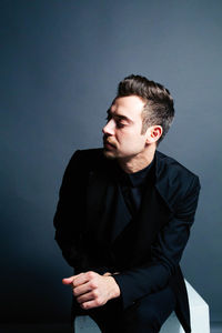 Young businessman sitting against gray background