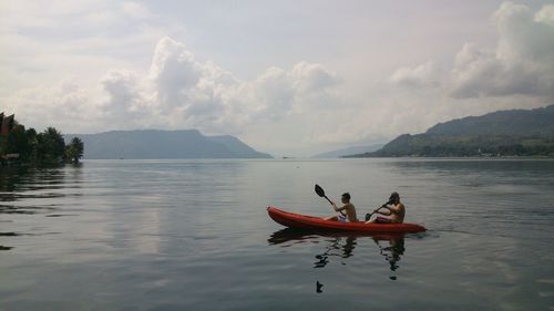 People canoeing on lake against sky