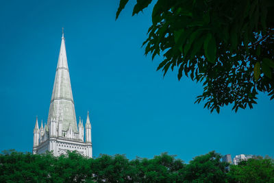 Low angle view of trees and building against blue sky