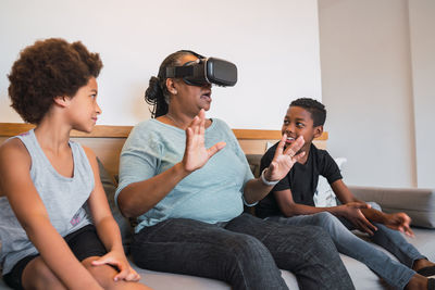 Grandmother using virtual reality goggles while sitting on sofa with kids at home