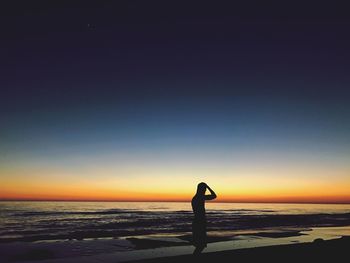 Man standing on beach against clear sky at sunset