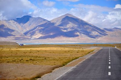 Empty road by field against mountains